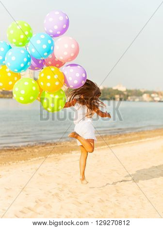 Happy little girl playing with balloons at the beach