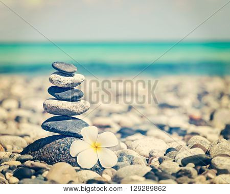 Zen meditation spa relaxation background - vintage retro effect filtered hipster style image of balanced stones stack with frangipani plumeria flower close up on sea beach