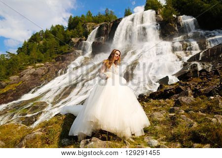 bride posing near the norvegian waterfall with blue skies