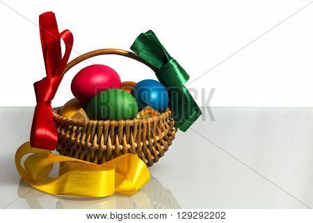 Easter Wicker basket with pink vines painted chicken eggs on a white background and on the basis of reflective matte decorated with colorful ribbons.