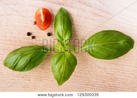 Basil leafs and quarter of cherry tomato on wooden cutting board