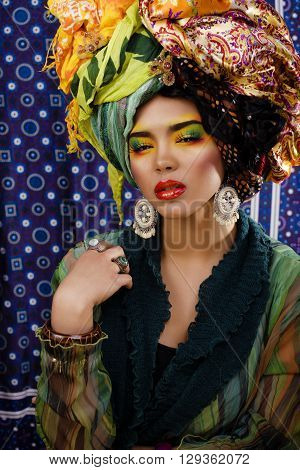 beauty bright woman with creative bright make up, many shawls on head like cubian, ethno look closeup