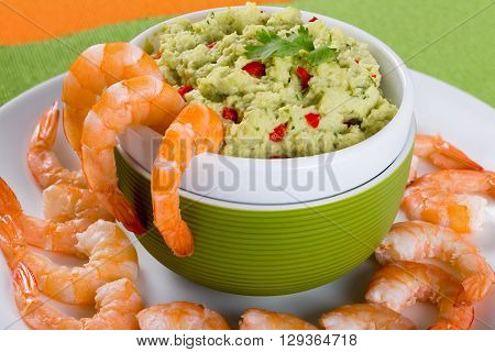 boiled tiger prawns tails on a white plate with guacamole sauce in a green bowl on a table mat on an old rustic table studio lights close-up