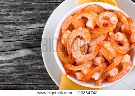boiled tails of king shrimps on a white bowl on a dish with orange table napkin on an old rustic tabletop view studio lights