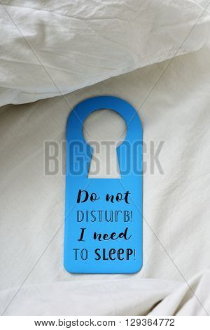 closeup of a blue door hanger with the text text do not disturb I need to sleep written in it, placed on a comfortable bed