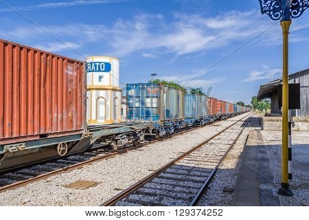Crato, Portugal. July 2, 2015: A freight train from Comboios de Portugal (Portuguese Trains) passing by a deactivated Railroad Station in the interior south of Portugal.