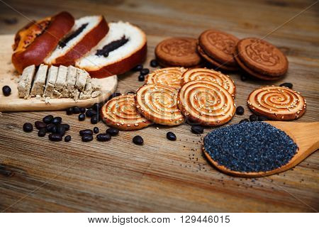 There are Pieces of Roll with Poppyseed,Cookies and Halavah,Chocolate Peas.Tasty Sweet Food on the Wooden Background
