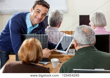 Smiling Teacher Showing Digital Tablet To Senior Students In Cla
