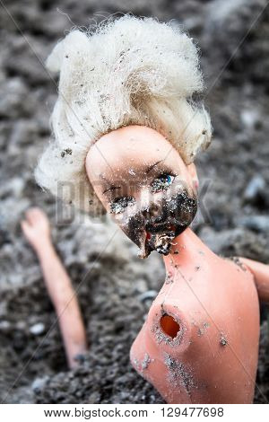 Dirty creepy plastic doll in the pile of grey ash