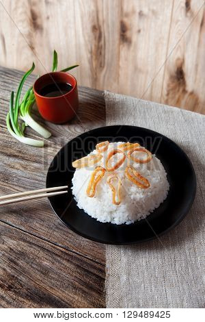 Spicy stir fried squid with rice and green onion and chopstick on black bowl on rustic brown wooden background
