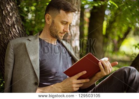 mature man reading book under the trees in park