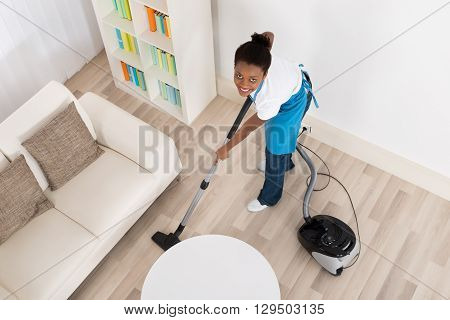 High Angle View Of Young African Female Janitor Cleaning Hardwood Floor With Vacuum Cleaner