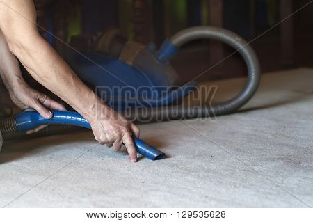 Male hands with a vacuum cleaner carefully removing a dust from a carpet indoor shot with selective focus