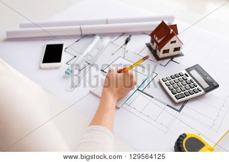 business, architecture, building, construction and people concept - close up of architect hand with blueprint and architectural tools writing to notebook