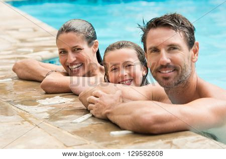 Pretty little girl with her parents in swimming pool. Happy family smiling and looking at camera in swimming pool. Portrait of a happy couple with daughter in swimming pool.