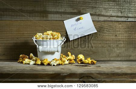 White bucket with popcorn on wooden background