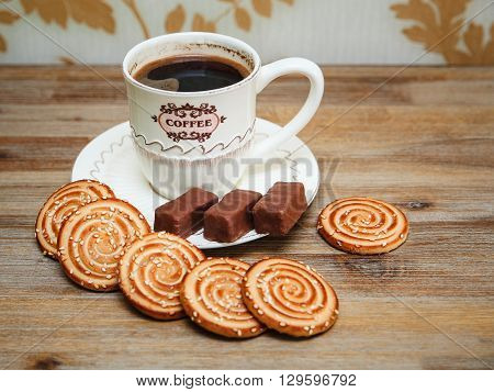There are CookiesбChocolate Candy Porcelain Saucer and Cap with CoffeбTasty Sweet Food on the Wooden Background