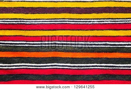 Multicolored handmade woollen rug texture with parallel stripes in red yellow black white and orange in a closeup full frame view