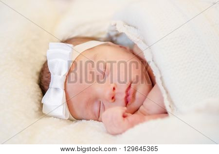 A baby girl in white headband is sleeping covered with a white blanket