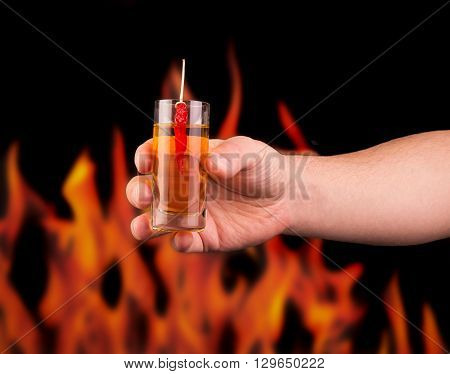 Hand holds a glass of pepper vodka on a background of flame