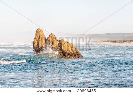 A lone rocky outcrop enduring the waves in an early morning scene at a beach at Buffelskop near Knysna.