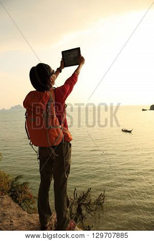 young woman hiker use digital tablet on sunset seaside