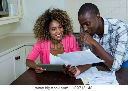 Happy couple checking bills while using digital tablet in kitchen