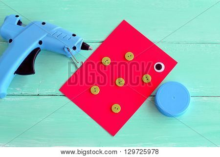 Hot glue gun. A cap from a plastic bottle, buttons, cardboard sheet, a plastic eye - set for making children's crafts fish. Project to make from recycling bottle caps. Kids art