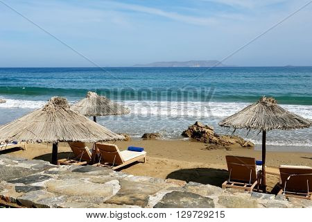 Landscape with umbrellas on the beach island and Mediterranean sea with waves Crete Greece.