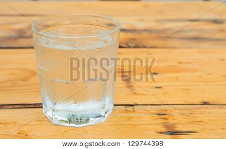 Glass water with iceDrops water on glass placed on wooden table.