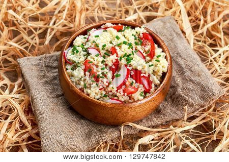 Homemade Fresh Couscous salad with vegetables wooden bowl on straw