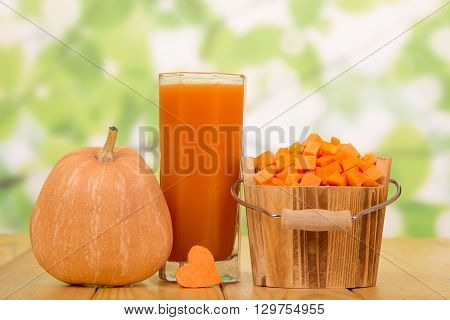 Ripe pumpkin bucket with dice and a glass of juice on the abstract green background.