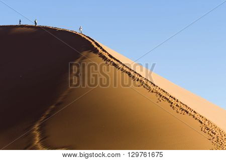 People walking on the crest of a red dune in the Namib Desert in Sossusvlei in the Namib-Naukluft National Park of Namibia