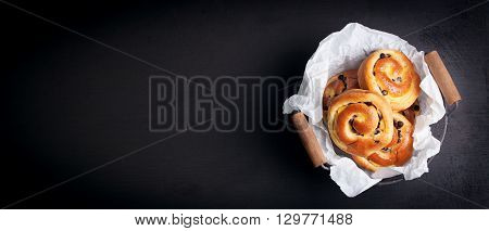 Fresh baked vanilla sweet sugar buns with chocolate drops in a crate on a black wooden background, top view, with free space for text, vertical