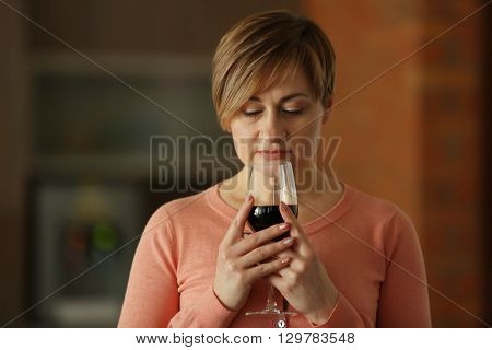 Beautiful middle-aged woman tasting red wine, indoors