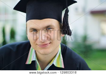 The young man with a smile looking at the camera. He has an academic cap on his head
