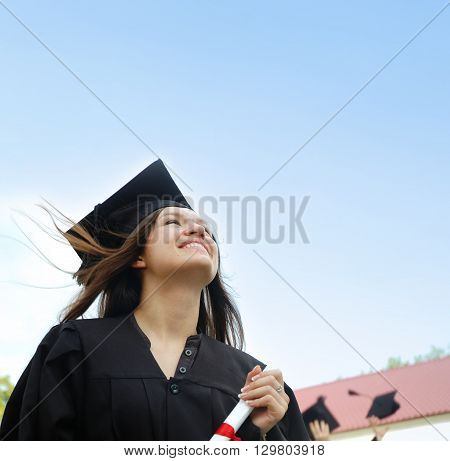 Student in cap and gown looking up at the blue sky background