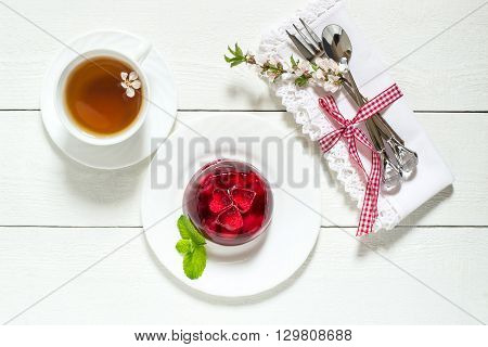 Delicious cherry jelly with whole berries on a plate tea and blooming cherry branch on a white wooden background