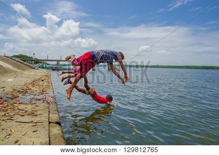 Muisne, Ecuador - March 16, 2016: Kids diving and swimming in pacific ocean from stone surface with clothes on.
