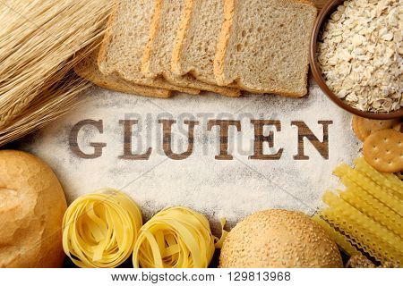 The word GLUTEN and flour products on wooden surface closeup