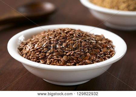 Brown flax seeds or linseeds in small bowl photographed on dark wood with natural light (Selective Focus Focus one third into the seeds)