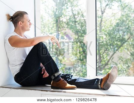 Handsome young man sitting on windowsill 