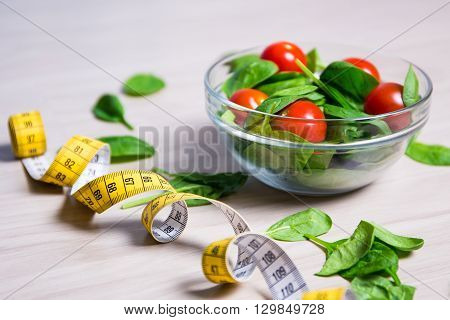 Diet And Weight Loss Concept - Healthy Salad With Spinach And Tomatoes And Measure Tape