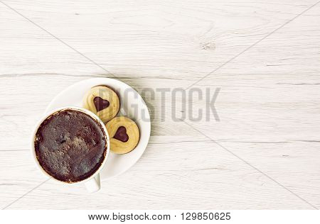 Cup of black coffee with two jam biscuits in the shape of heart on the wooden background. Place for text in right. Food and drink. Sweet delight. Retro filter.