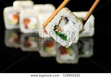 close up of chopsticks taking portion of sushi roll on the table restaurant / eating sushi roll using chopsticks