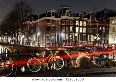 AMSTERDAM NETHERLANDS - 17TH FEBRUARY 2016: A view of bridges buildings and bikes at the Leidsegracht and Keizersgracht canal intersection in Amsterdam at night. The trail from traffic can be seen.