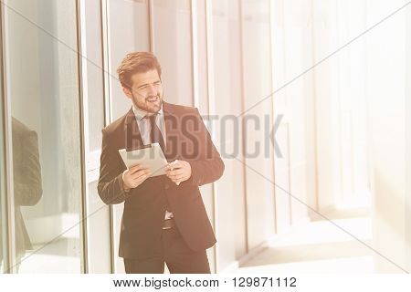 Toned image of businessman or freelancer walking along street with tablet PC in his hands. Happy man in business suit looking away in distance.