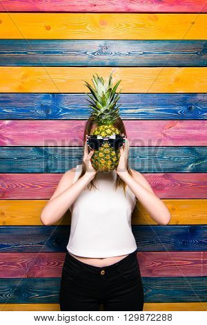 Girl holds pineapple in front of the face. Young girl on a colorful striped background. Fruit fashion girl. Bright juicy picture