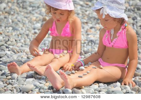 duas menininhas é brincar com pedras de seixo. foco em menina com Chapéu Panamá branco na cabeça.