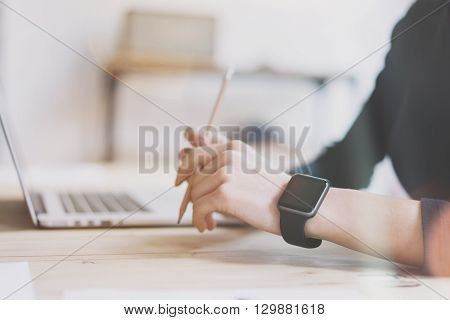 Photo Girl Working Modern Laptop in Studio Loft. Woman Wearing Generic Design Smartwatch.Account Manager Work Process. Notebook on the Wood Table.Horizontal mockup.Burred background. Visual effects.
